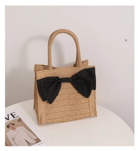 Close-up of woven straw handbag featuring a large black fabric bow on a white table