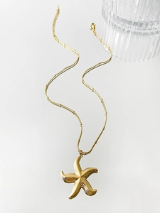 Close-up of golden starfish necklace with textured pendant on a minimalist white surface
