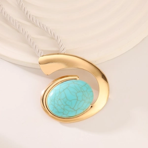 Close-up of golden spiral pendant with turquoise gemstone on white woven cord