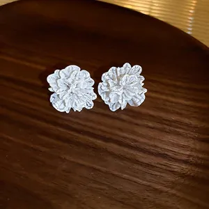 Elegant white floral stud earrings with vintage crackle effect on dark wood background