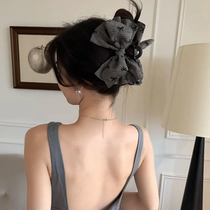 Large grey fabric bow hair claw clip with black pattern worn by model in elegant setting
