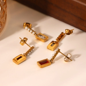 Golden stud earrings with rectangular gemstones and pearl accents on vintage wood
