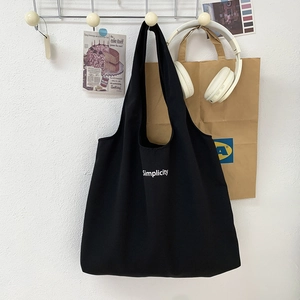 Détail d'un sac cabas noir en toile avec lettrage Simplicity blanc sur un crochet mural