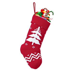 Detail of red knitted Christmas stocking with white tree patterns and festive gift fillers