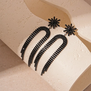 Détail de boucles d'oreilles sombres avec nœud, fleurs, strass noirs et pompons