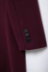 Détail de la manche d'un manteau bordeaux avec quatre boutons noirs et texture sergé