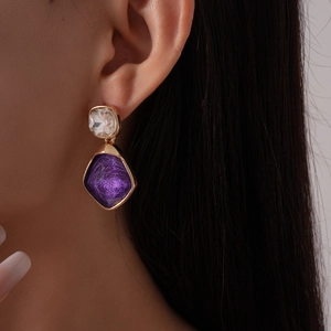 Dettaglio orecchini vintage in resina con trama a rombi viola e cornice dorata su modella