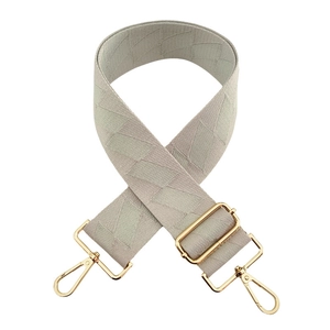 Detail of beige quilted fabric bag strap with adjustable gold buckles on white background