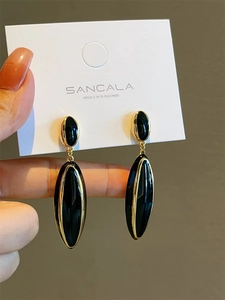 Close-up of elegant gold-plated drop earrings with black enamel inlay on a display card