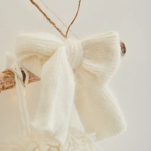 Handcrafted cream white knitted bow decoration hanging on a wooden branch for Christmas