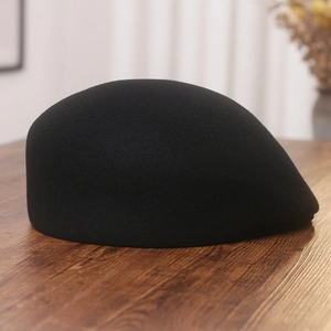 Detail view of a black wool felt beret hat on a natural wooden texture background
