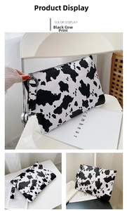 Detail view of the black and white cow print clutch bag with zipper and wrist strap