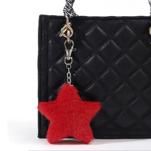 Red plush star bag charm with silver clip attached to a black quilted leather handbag