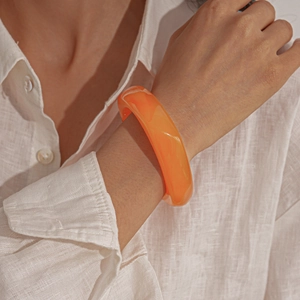 Detail of chunky orange translucent resin bangle worn against a white linen shirt