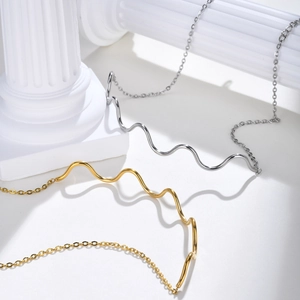 Elegant gold and silver wave-shaped stainless steel necklaces on a white column