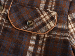 Close-up of brown plaid wool coat fabric with buttoned pocket and refined texture