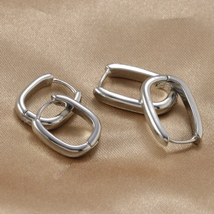 Detailed view of silver geometric hoop earrings set on soft brown satin fabric background