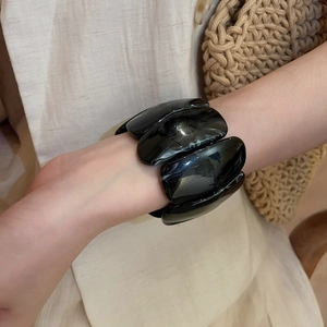 Detail of a chunky black acrylic bracelet worn on wrist with minimalist beige background