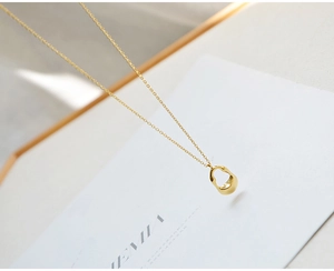 Detail of minimalist hollow teardrop pendant on thin gold chain against white background