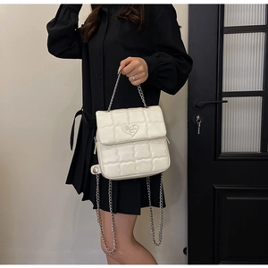 Detail of white quilted crossbody bag with metal chain strap and heart hardware