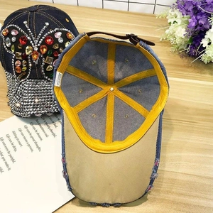 Detail of denim baseball cap showing colorful rhinestone butterfly and distressed edges