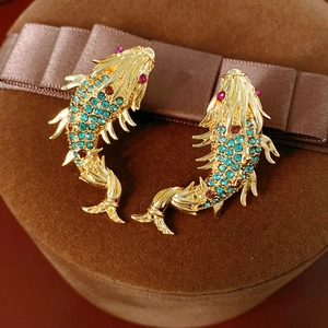 Macro detail of vintage gold fish earrings with blue and red pavé crystals on velvet box