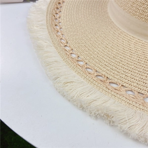 Dettaglio del cappello di paglia beige con trama traforata e bordi con frange