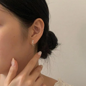 Close-up of a minimalist silver bow earring worn by a model in soft lighting