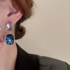 Close-up of model wearing geometric gold earrings with purple and blue crystals