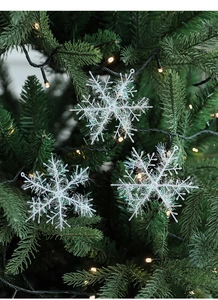 Close-up of white snowflake ornaments with iridescent tinsel on green Christmas tree