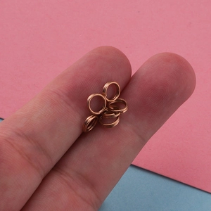 Macro shot of small rose gold stainless steel split rings on a fingertip for size scale