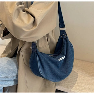 Close-up of denim crescent shoulder bag with white fashion label on khaki trench coat