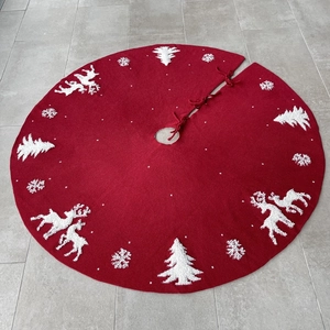 Close-up of red knitted Christmas tree skirt with white tufted elk and snowflake patterns