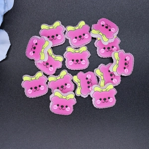 Flat lay of shiny pink resin bear charms with yellow bows for DIY crafts and decor
