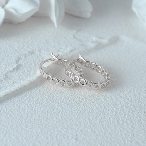 Macro shot of S925 sterling silver infinity hoop earrings on a marble surface