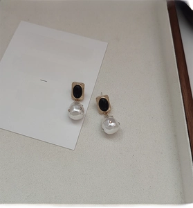 Dettaglio di orecchini vintage dorati con perle barocche, accenti neri e piccoli strass