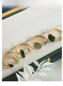 Detailed view of four vintage gold rings with emerald and blue enamel on green velvet box