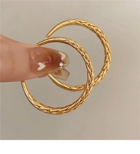 Close-up of large gold twisted hoop earrings with detailed woven texture on fingers
