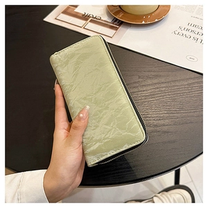 Long mint green velvet wallet with zip closure held by model on dark wooden table