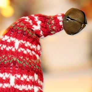 Close-up of red and white knitted Christmas doll hat with a vintage metal bell detail