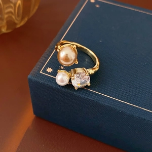 Détail d'une bague dorée avec perle champagne et oxyde de zirconium sur écrin bleu