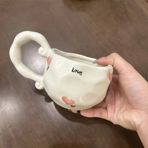 Detail of a wavy handle ceramic coffee cup with red hearts and Love lettering art
