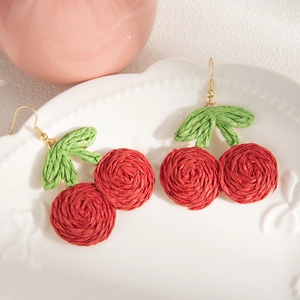 Detail of handmade woven cherry earrings with red fruit and green leaves on a white tray