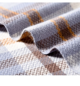 Macro shot of thick plaid scarf fabric showing soft cashmere texture and grey orange weave