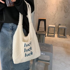 Detail der weißen Plüschtasche mit blauer Luck-Stickerei und weicher Lammwoll-Textur