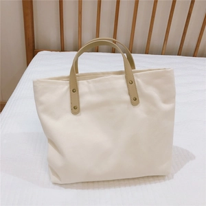Close-up of the beige canvas tote bag with khaki leather handles and gold metal rivets