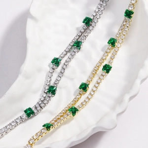 Macro detail of gold and silver tennis chains with emerald-cut green gems and pavé zircons