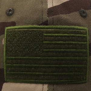 Close-up of the American flag embroidered patch on a camouflage canvas baseball cap