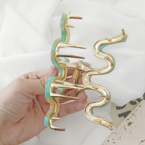 Handheld view of a large golden wave-shaped snake hair claw with mint green acetate inserts