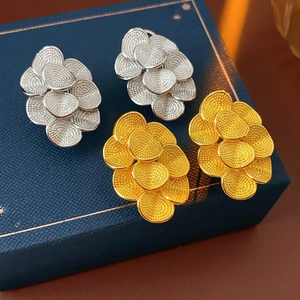 Détail macro de boucles d'oreilles fleurs plaquées or 18K et argent au fini mat texturé